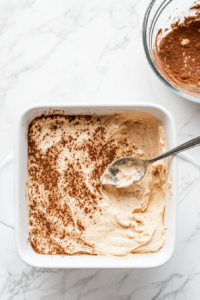 This image shows spoonfuls of a rich, cinnamon-sugar mixture being dropped onto the cake batter, adding layers of flavor and sweetness.