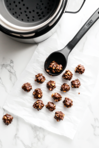 This image shows spoonfuls of chocolate-coated peanuts being dropped onto parchment paper, forming individual clusters ready to set.