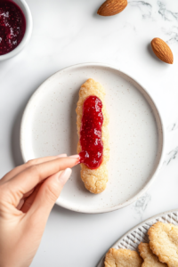 This image shows the fully baked witch finger cookies with almond "nails" in place, finished with red jam drizzled on top to mimic dripping blood for a spooky Halloween effect.