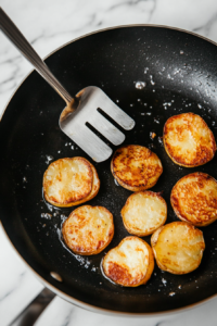 This image shows tongs flipping the potato stacks in the pan, ensuring both sides are evenly crispy and golden.