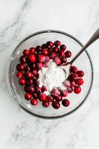 This image shows fresh cranberries being tossed in flour to prevent them from sinking to the bottom of the cranberry orange loaf during baking.