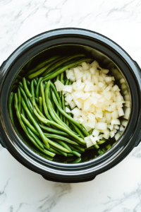 This image shows fresh green beans being placed into the slow cooker, ready to soak up the savory flavors of the broth and seasonings.