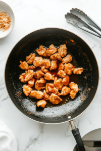 This image shows pieces of chicken being deep-fried in a wok, sizzling in hot oil until they turn crispy and golden brown.