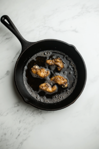 This image shows chicken pieces being fried in hot oil until they achieve a crispy, golden-brown exterior.