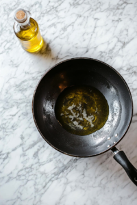 This image shows a wok filled with hot oil heating up, preparing for frying the marinated chicken to crispy perfection.