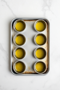 This image shows hot oil sizzling in a muffin tin, getting ready for the Yorkshire pudding batter to be poured in, ensuring a crispy and golden finish.