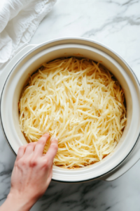 This image shows a layer of shredded hash browns evenly spread in the crockpot, forming the crispy base for the breakfast casserole.