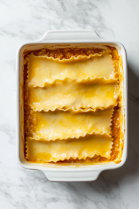 This image shows a layer of lasagna pasta sheets being placed over the cheese mixture, starting the layering process of Buffalo Chicken Lasagna.