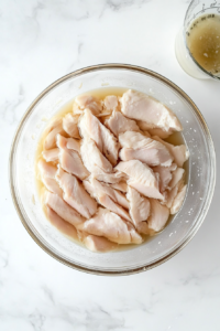 This image shows chicken pieces soaking in a flavorful marinade, infusing them with rich taste before frying for the sandwich.