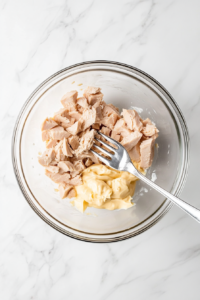 This image shows a top-down view of tuna being combined with creamy mayonnaise in a mixing bowl, forming the base of a delicious tuna salad.