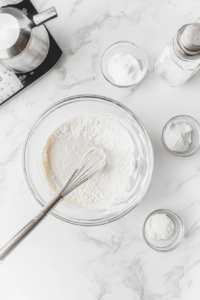 This image shows a small bowl of powdered sugar, milk, and vanilla extract being whisked together to create a smooth and sweet glaze for drizzling over the cake.