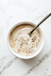 This image shows cream of mushroom soup, milk, salt, and pepper being stirred together in a mixing bowl until smooth and fully blended, forming the creamy base for the green bean casserole.