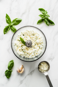 This image shows finely minced garlic and a splash of lemon juice being added to the whipped feta mixture, enhancing its depth of flavor.