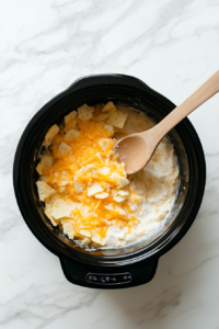 This image shows the ingredients being stirred together in the crockpot, ensuring the potatoes are evenly coated with cheese and seasonings for a rich, consistent flavor.