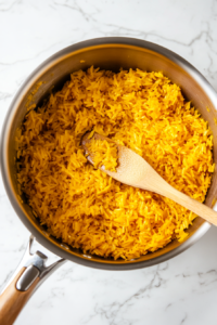 This image shows rice being stirred together with turmeric in a pan, evenly coating the grains with the bright golden spice.