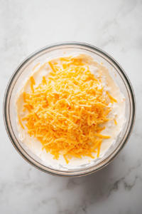 This image shows a bowl with ricotta cheese, shredded cheese, and seasonings being mixed together, forming the creamy cheese mixture for Buffalo Chicken Lasagna.