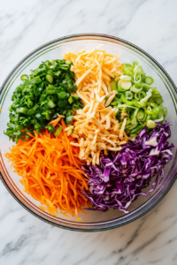 This image shows a large bowl filled with shredded chicken, crunchy red cabbage, and crisp carrots, ready to be combined for a colorful and refreshing Chinese chicken salad.