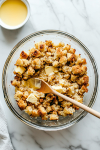 This image shows stuffing being combined with melted butter in a bowl, creating a buttery, flavorful mixture to top the casserole.