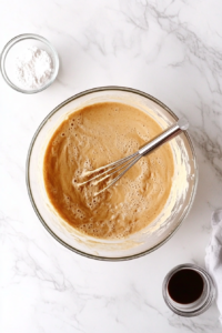 This image shows a mixing bowl filled with ingredients being whisked together to create the smooth and creamy bottom layer batter for the Cinna-Bun Cake.