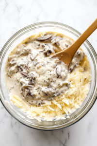 This image shows the process of mixing the ingredients for the sauce in a large glass bowl, creating a creamy mixture for the Crockpot Hashbrown Casserole.