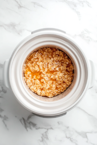 This image shows oatmeal cooking in the crockpot, with tender apple slices on top, as it simmers to a creamy, flavorful consistency.