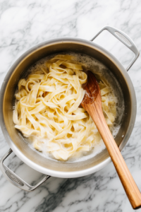 This image shows a pot of boiling water with pasta cooking until tender, the first step in preparing the dish.