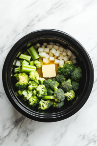 This image shows freshly chopped broccoli and other key ingredients being added into a crockpot, getting ready for the slow cooking process to make a rich and creamy soup.