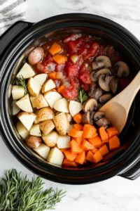 This image shows fresh vegetables and seasonings being added to the slow cooker, preparing for a rich and hearty stew.