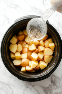 This image shows whole potatoes being added into a slow cooker, ready to be cooked for the mashed potato recipe.