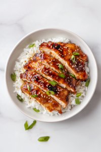 This image shows sliced teriyaki chicken served over rice, garnished with fresh scallions and sesame seeds for a final touch of flavor and presentation.