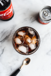 This image shows Coca-Cola being poured into a glass with whiskey, creating a fizzy and well-mixed cocktail.