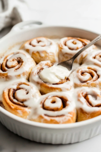 This image shows warm cinnamon rolls being drizzled with rich and creamy cream cheese icing, adding the perfect finishing touch.