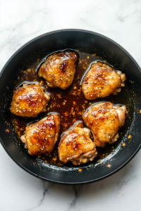 This image shows thick teriyaki sauce being poured over cooked chicken, coating it in a rich, glossy glaze.