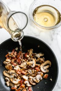 This image shows a generous pour of white wine and chicken stock being added to the pan, creating a fragrant and flavorful sauce for the chicken casserole.