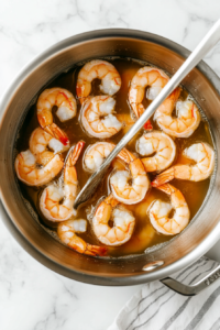 This image shows a variety of aromatic spices being sprinkled into the bubbling water, creating a flavorful base that infuses the shrimp with rich and savory seasoning.