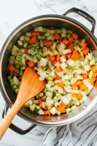 This image shows chicken pieces and fresh herbs being combined with a rich broth in a pot, preparing the soup for simmering and infusing flavors.