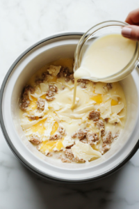 This image shows the whisked egg mixture being poured over the layers of hash browns, sausage, and cheese, binding everything together.