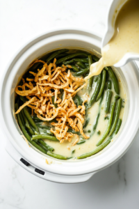 This image shows the creamy green bean casserole mixture being transferred from a mixing bowl into a Crockpot, ready to be slow-cooked to perfection.