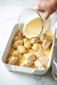 This image shows the thick, creamy sauce being poured generously over the arranged chicken pieces in the casserole dish, coating them for a flavorful bake.