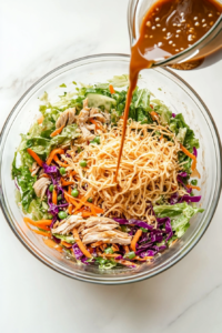 This image shows a rich, flavorful dressing being drizzled over a bowl of Chinese chicken salad, coating the fresh ingredients for a deliciously balanced taste.