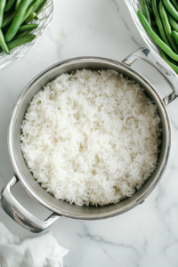 This image shows fluffy cooked rice and vibrant steamed green beans being prepared as side dishes for the honey bourbon chicken.