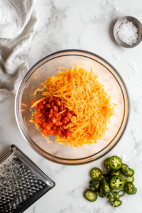 This image shows a bowl of freshly mixed pimento cheese, made with shredded cheese, diced pimentos, and seasonings, ready to be spread on the sandwich.