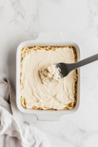 This image shows additional layers of pasta, cheese mixture, and buffalo chicken being added to the baking dish, building up the lasagna.