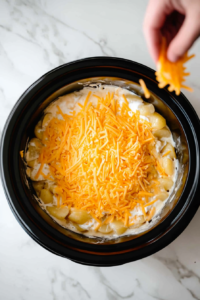 This image shows the layering process being repeated with more sliced potatoes, creamy sauce, and shredded cheese, building up the dish for even cooking.