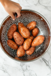 This image shows sweet potatoes being rinsed under running water to remove any dirt and debris before placing them in the slow cooker.