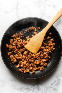 This image shows ground sausage browning in a skillet, releasing its savory aroma as it cooks for the casserole.