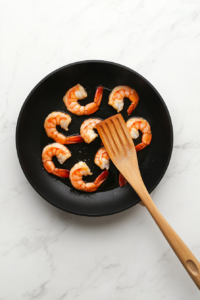 This image shows shrimp sizzling in a hot pan, turning golden and tender as they cook to perfection for the Bang Bang Chicken and Shrimp recipe.