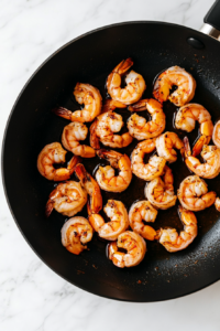 This image shows shrimp sizzling in a hot pan with butter, turning pink and tender as they cook to perfection for the creamy shrimp rigatoni.