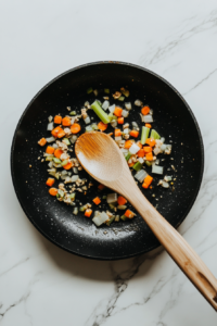 This image shows a skillet filled with diced carrots and peas being sautéed to soften and enhance their flavor.