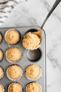 This image shows a spoon or scoop filling a mini muffin tin with cornbread batter, ensuring even portions for baking.